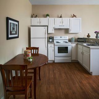 A cozy kitchen with white cabinets, a dining table, and wooden flooring.