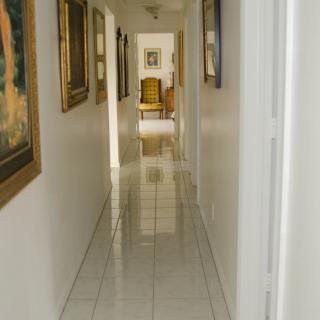 A long hallway with tiled flooring and artwork on the walls leading to a distant chair.