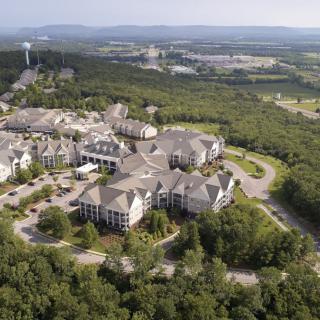 Aerial view of a large building complex surrounded by lush greenery and forested areas, with roadways connecting the structures.