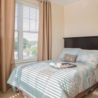 A cozy bedroom with a single bed, decorated with soft bedding and a tray, illuminated by natural daylight streaming through the window.