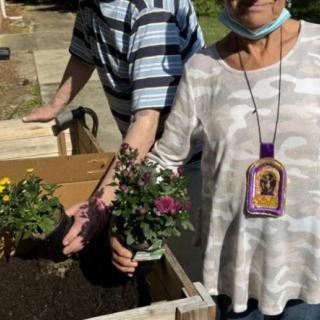 Two people planting flowers in a garden bed outdoors.