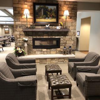 A cozy living room with comfortable armchairs surrounding a stone fireplace, adorned with a decorative painting and soft lighting.