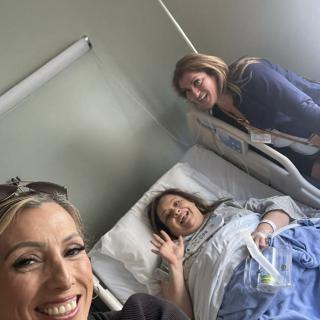 Three women smiling, with one lying in a hospital bed.