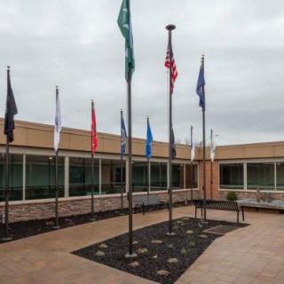 A courtyard with multiple flagpoles displaying various flags outside a building on a cloudy day.