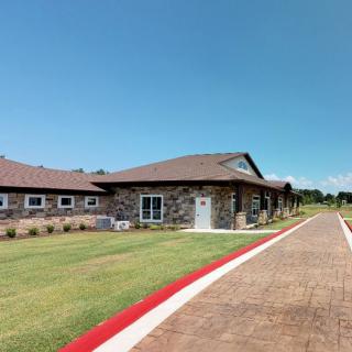 A modern single-story building with a stone facade surrounded by a green lawn and clear blue sky.