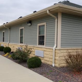 A building with green siding, white trim, and landscaped surroundings.