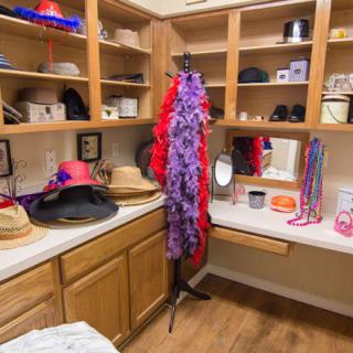 A closet corner filled with colorful hats and accessories, featuring a feather boa and a vanity mirror.