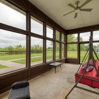 A cozy sunroom with large windows, featuring a red swing and outdoor views.