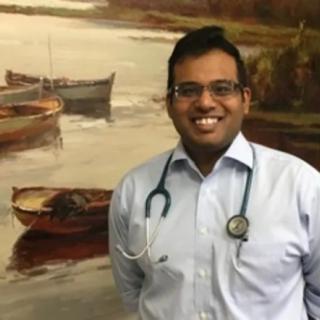 A smiling doctor stands in front of a painting featuring boats on the water.
