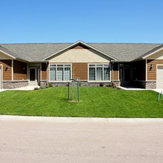 A picturesque duplex with a well-maintained lawn under a clear blue sky.