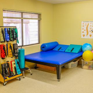 A well-equipped therapy room featuring a blue mat, exercise balls, and various physical therapy tools.