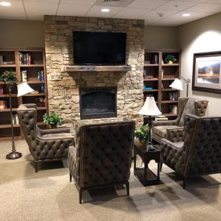 A cozy living room with a stone fireplace, surrounded by bookshelves and elegant chairs.
