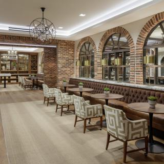 Elegant restaurant interior with brick walls and arched windows, featuring comfortable seating and chandeliers.