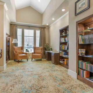 A cozy library setting with bookshelves, comfortable chairs, and large windows.