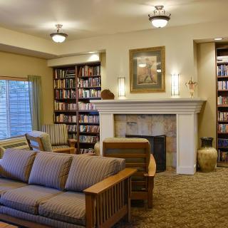 A cozy library room with bookshelves, a fireplace, and comfortable seating.