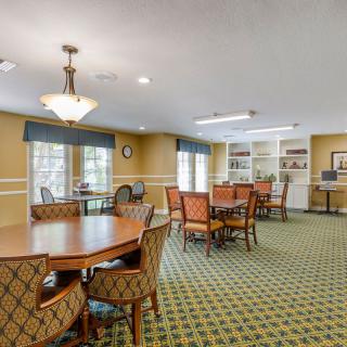 A spacious dining room with multiple tables and chairs, featuring large windows, bookshelves, and elegant lighting.
