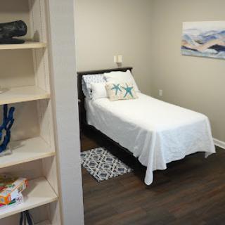 A cozy and minimalist bedroom featuring a single bed with white bedding, decorative pillows, and a stylish shelf.