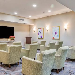 A modern conference room setup with comfortable chairs facing a large television and podium, decorated with artwork on the walls.