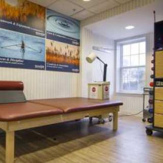 A therapy room with a massage table, wall posters, and a lamp next to a window.