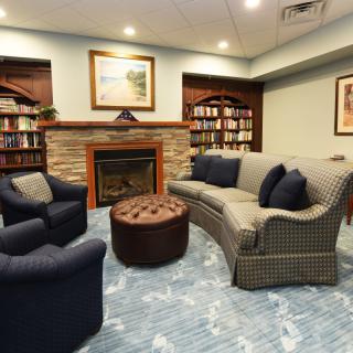 A cozy reading room with a fireplace, sofa, and bookshelves.