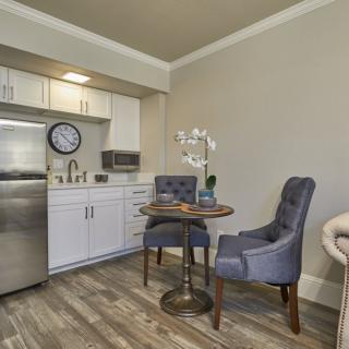 A modern kitchenette with a small dining area featuring two upholstered chairs and a round table.