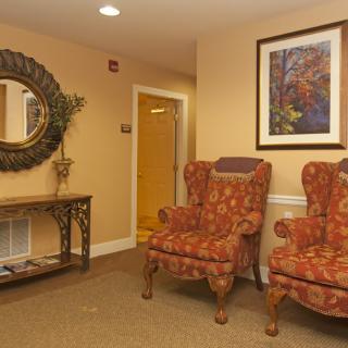 A cozy lobby area with two patterned armchairs, a decorative mirror, and a framed painting.