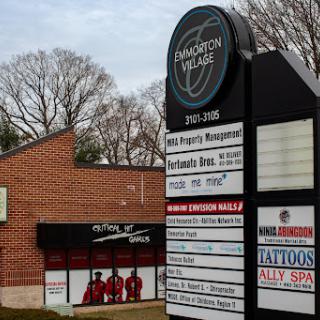 A view of a shopping center sign listing various businesses, including property management and a tattoo shop.