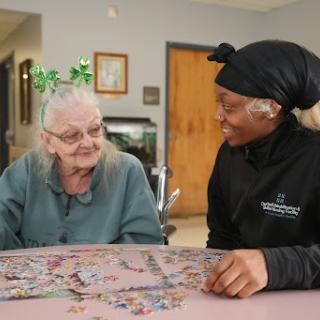 A caregiver and an elderly woman enjoy a joyful moment together while working on a puzzle.
