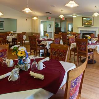 A cozy dining room with neatly set tables, adorned with flowers and surrounded by elegant wooden chairs.