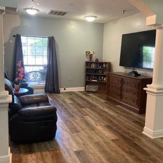 A cozy living room with hardwood flooring, a large television mounted on the wall, a comfortable couch, and a bookshelf next to a window with curtains.