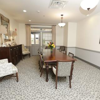 A well-furnished dining room with a wooden table and chairs, decorated with a floral centerpiece, and illuminated by chandeliers.
