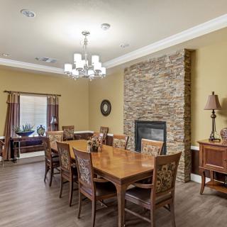 A cozy dining room featuring a large wooden table, a stone fireplace, and elegant lighting.
