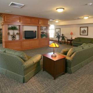 A cozy living room with green sofas facing a television and a wooden coffee table topped with a lamp.