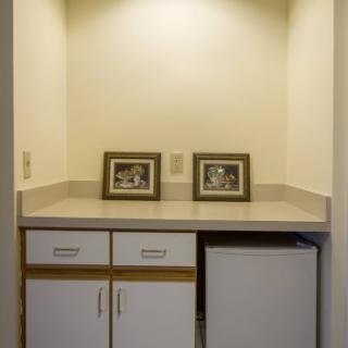 A small kitchenette area featuring framed photographs on a countertop, below which is a set of drawers and a refrigerator.