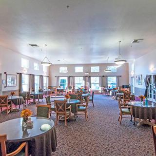 A spacious dining room with multiple tables and chairs, well-lit with large windows.