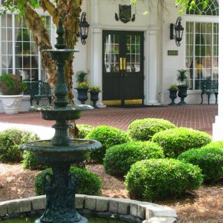 A charming building entrance with a fountain surrounded by neatly arranged bushes and greenery.