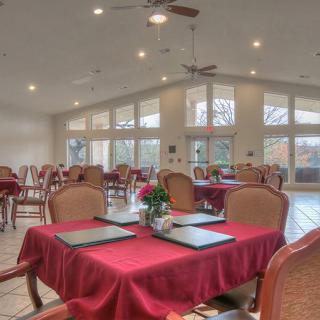 A spacious restaurant dining area with red tablecloths and large windows letting in natural light.