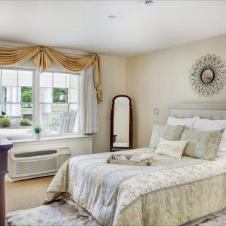 A cozy, well-decorated bedroom with a large bed, ornate mirror, and sunlit window.