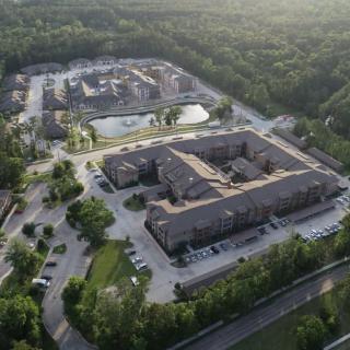 An aerial view of a residential complex surrounded by lush greenery and parking areas.