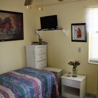A cozy bedroom featuring a colorful quilt, a small nightstand with flowers, and decorative art on the walls.