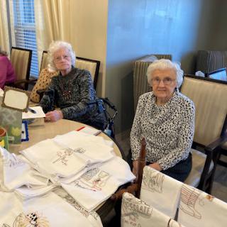 Two elderly women enjoying a crafting session at a communal table.