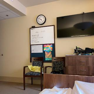 A quiet patient room in a hospital, featuring a clock, television, and comfortable seating area.