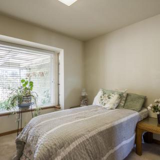A cozy, minimalist bedroom with ample natural light and a window seat adorned with plants.