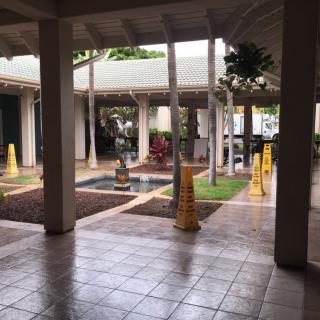 A serene courtyard with a central fountain, surrounded by a tiled floor and covered walkways, featuring several yellow caution signs.