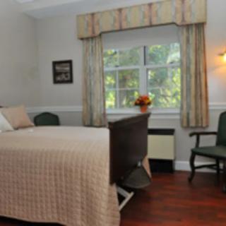 A cozy bedroom with a neatly made bed, two chairs, and a window with curtains overlooking greenery.