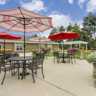 A sunny outdoor patio with tables, chairs, and red umbrellas.