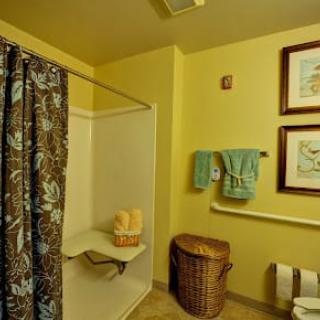 A cozy bathroom with yellow walls, featuring a shower with a patterned curtain, neatly hung towels, a wicker basket, and framed artwork on the wall.