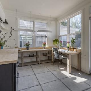 A bright sunroom filled with natural light, featuring large windows and a minimalist workspace adorned with plants.