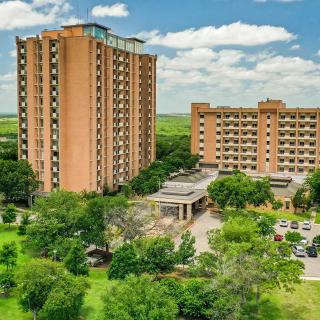 Aerial view of a hotel complex surrounded by lush greenery under a partly cloudy sky.