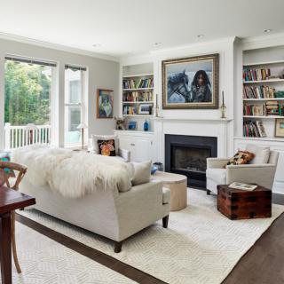 Cozy living room with a modern aesthetic, featuring a comfortable sofa, fireplace, and bookshelves filled with books, illuminated by natural light.